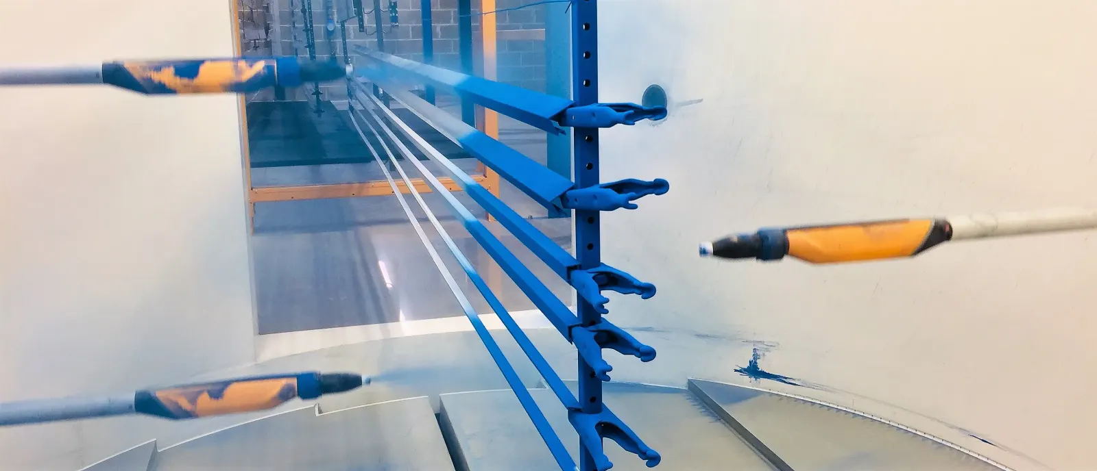 Automated spray guns applying blue powder to aluminium extrusions